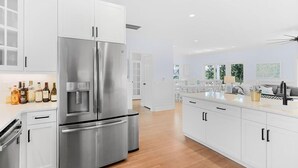 Una cocina moderna con armarios blancos, un refrigerador de acero inoxidable y piso de madera.