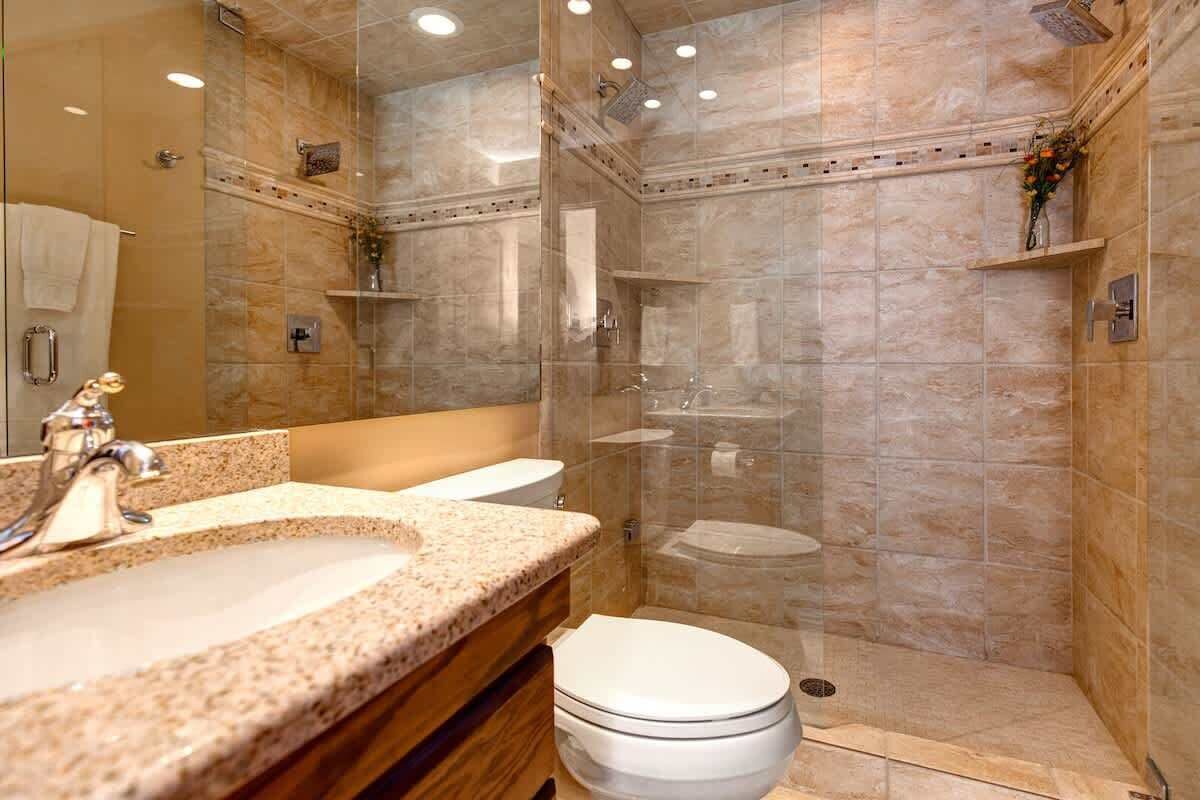 A bathroom with a granite countertop sink, a white toilet, and a glass-enclosed shower area.
