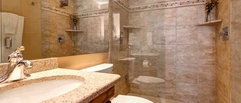 A bathroom with a granite countertop sink, a white toilet, and a glass-enclosed shower area.