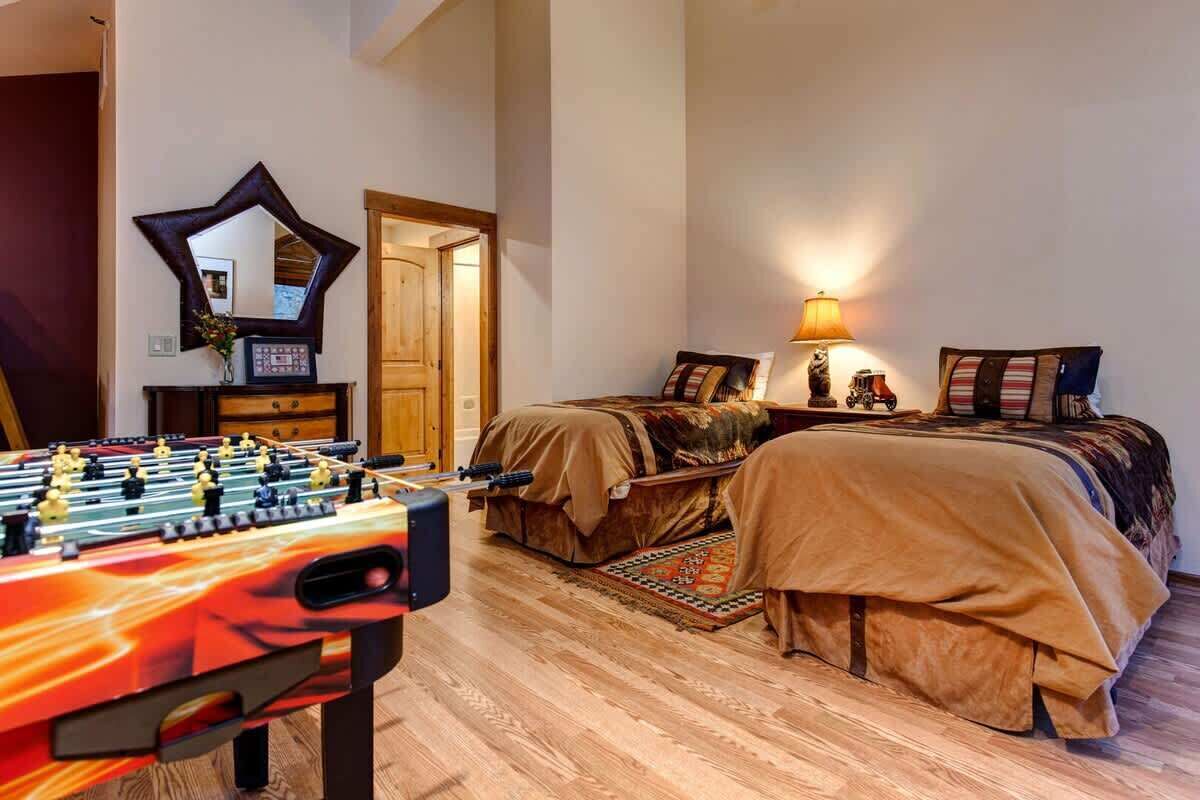 A room with a foosball table, a bed with a patterned blanket, a lamp, and a mirror on the wall.