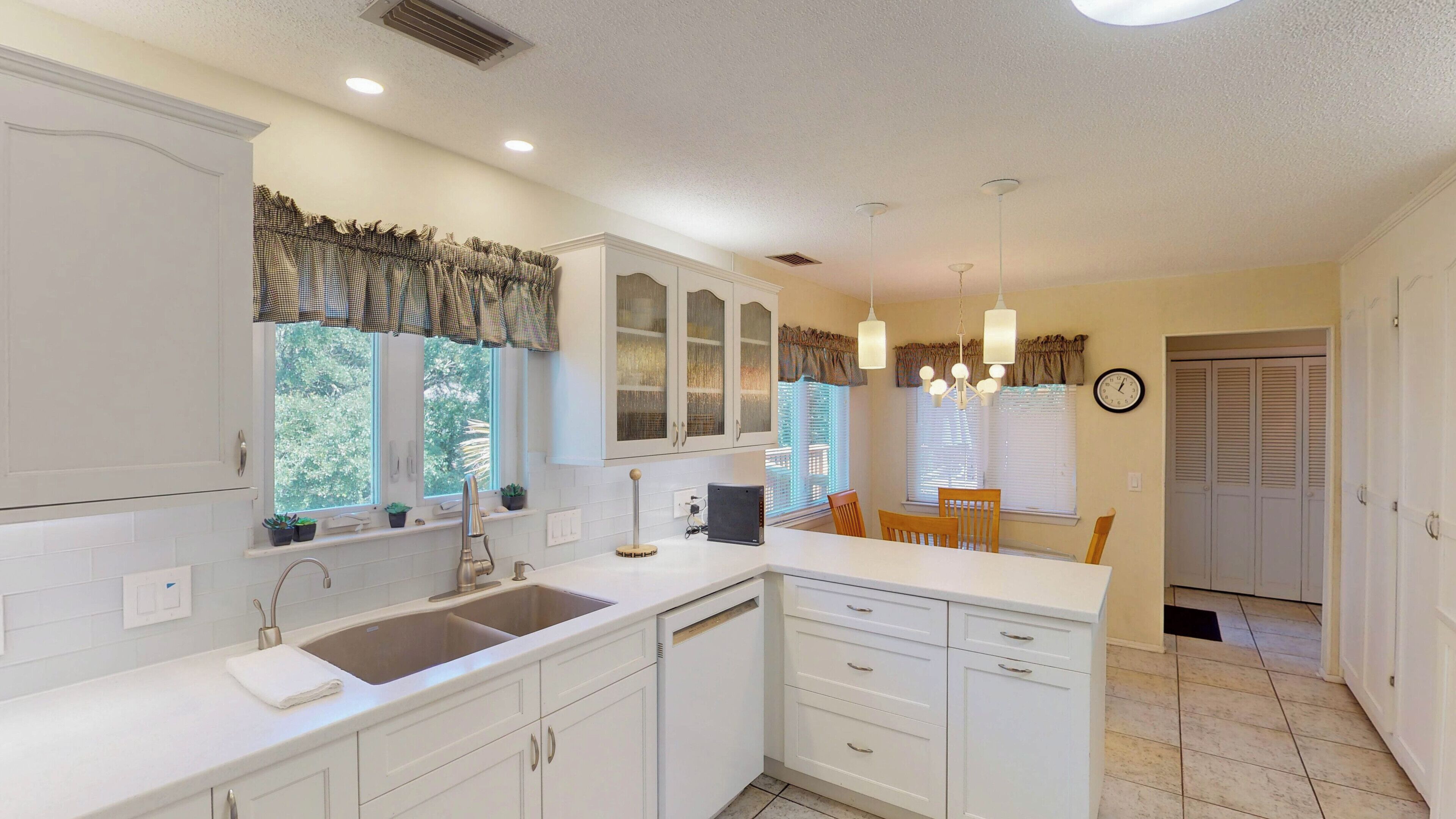 A kitchen with white cabinets, a double sink, and a dining area with a table and chairs.