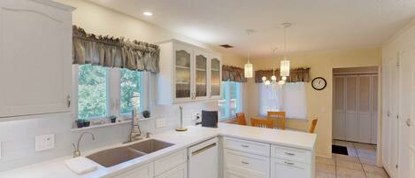 A kitchen with white cabinets, a double sink, and a dining area with a table and chairs.