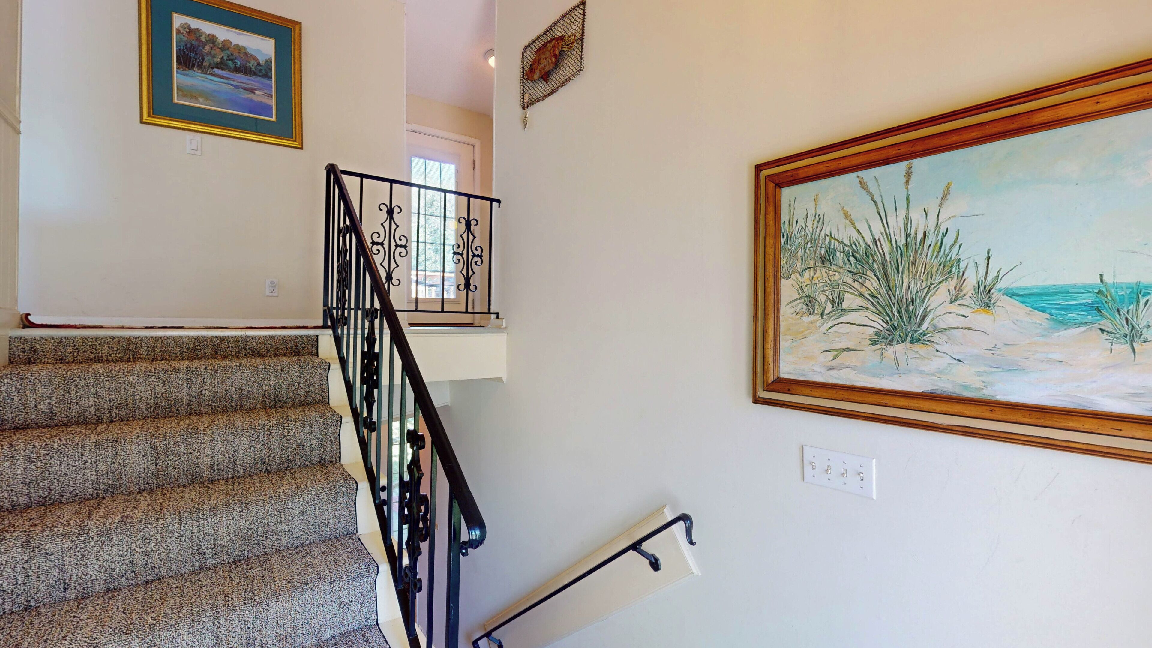 A staircase with a black railing, a painting of a beach scene, and a power outlet on the wall.