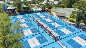 A rooftop tennis court complex with multiple courts, surrounded by residential buildings and trees.
