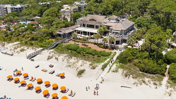 Luchtbeeld van een strandpand met een groot gebouw, een strand met parasols en een promenade die naar het gebouw leidt.