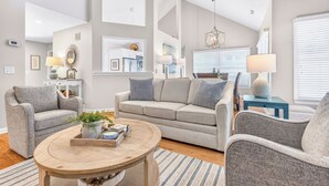 Een moderne woonkamer met een bank, fauteuils, een salontafel en een kroonluchter.
