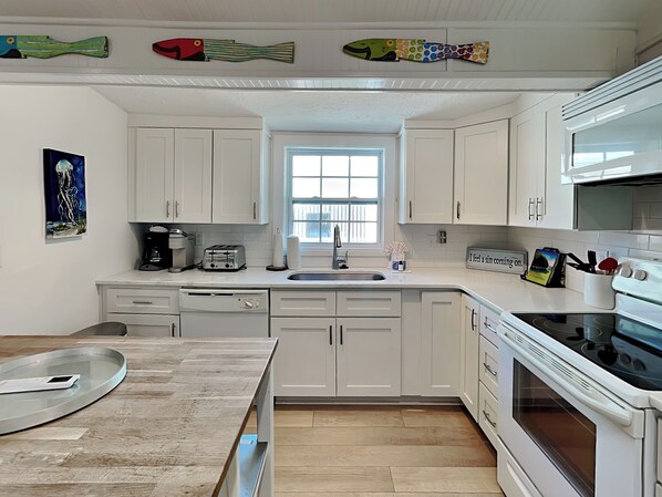 A kitchen with white cabinets, a window, a sink, a toaster, and a stove.