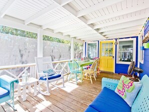 A covered outdoor area with a wooden deck, a yellow door, and a blue wall.