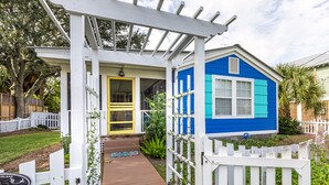 Una casa con fachada azul, un porche blanco y una puerta amarilla.