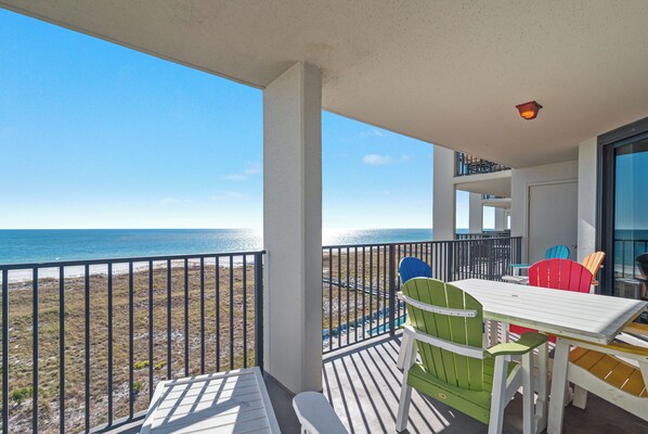 Un balcon avec vue sur la plage et l’océan, agrémenté d’une table et de chaises colorées.