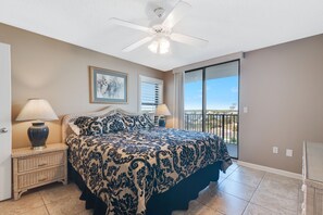 Une chambre avec un grand lit, deux tables de chevet, un ventilateur de plafond et un balcon avec vue.