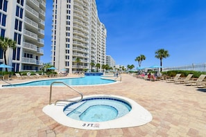 A hotel pool area with a hot tub, lounge chairs, and a large building in the background. - Beachfront Condo. Stunning Views from Balcony. (Destin)