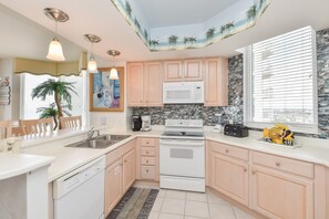Une cuisine moderne avec des meubles de couleur bois clair, un fourneau blanc et une grande fenêtre équipée de stores.