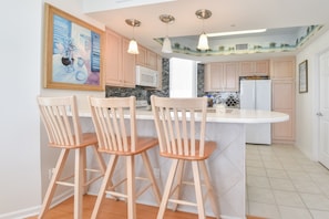 A kitchen with a central island, wooden bar stools, a painting on the wall, and a ceiling mural.
