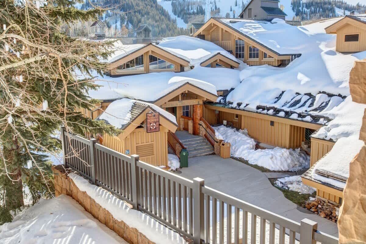 Un grupo de cabañas de madera con tejados nevados, una valla de madera y una vista despejada de las montañas circundantes.