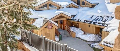 Un grupo de cabañas de madera con tejados nevados, una valla de madera y una vista despejada de las montañas circundantes.