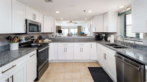 A modern kitchen with white cabinets, granite countertops, stainless steel appliances, and a black rug. - Surf Dweller 312🌊Gulf Front🏖️Free Beach Setup (Fort Walton Beach)