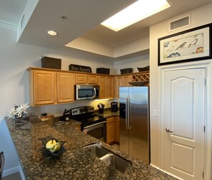 A modern kitchen with wooden cabinets, stainless steel appliances, granite countertops, and a framed artwork above the door.