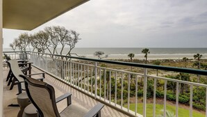 Un balcón con mobiliario exterior, con vista a una playa de vegetación escasa y al océano.