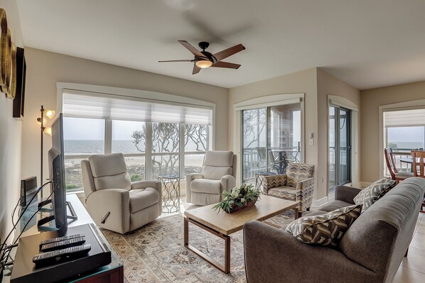 A spacious living room with a large window, a ceiling fan, and a television.