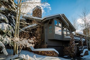 Casa revestida de piedra con chimenea de piedra, un garaje y un paisaje cubierto de nieve.