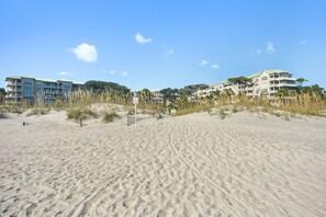 A sandy beach with footprints, a signpost, and buildings in the background.