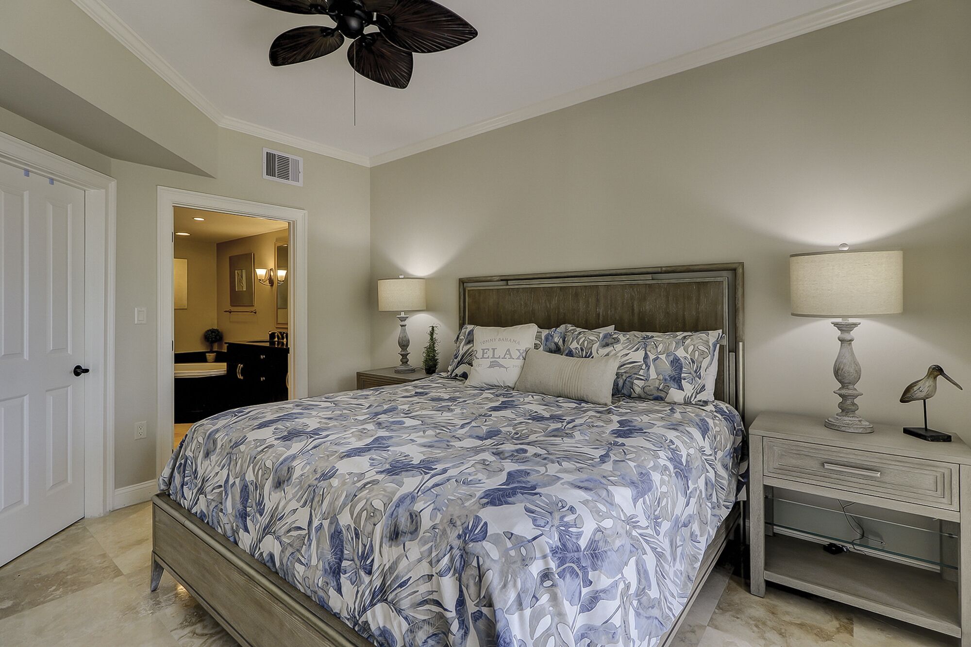 A bedroom with a bed, nightstands, a ceiling fan, and a door leading to a bathroom.