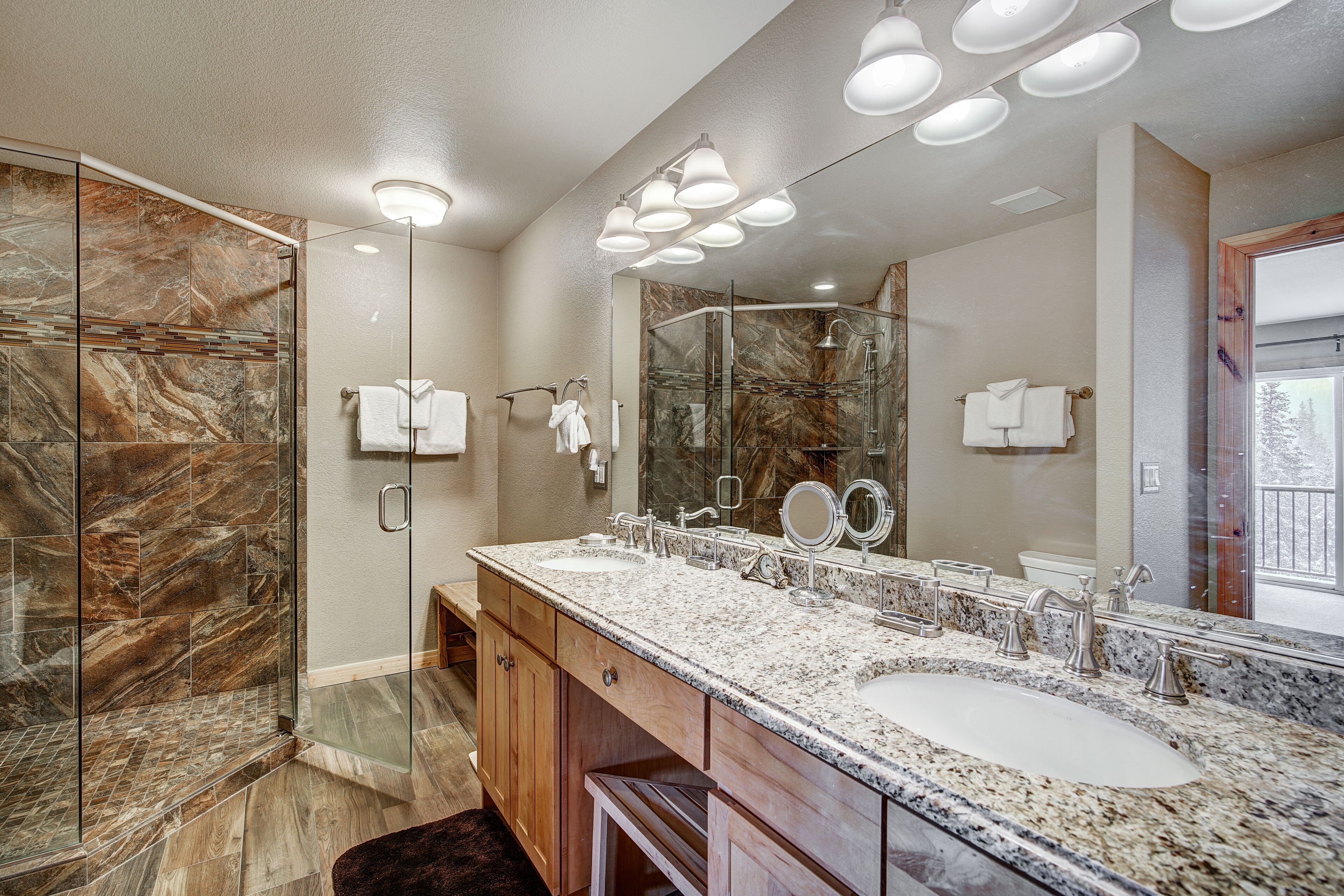 Un baño moderno con cabina de ducha de vidrio, un tocador amplio con encimera de granito y un espejo grande sobre el lavabo.
