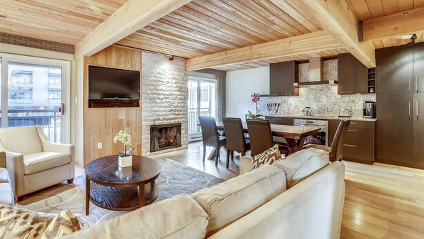 A spacious living area with a fireplace, a dining table, and a kitchen area with dark cabinets and a marble backsplash. - Elegant Downtown Chateau | Walk to Shop, Ski & Dine (Aspen)