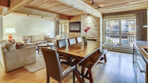 A spacious living room with a wooden dining table, leather chairs, a sofa, and a TV mounted on the wall. - Elegant Downtown Chateau | Walk to Shop, Ski & Dine (Aspen)