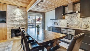 A modern kitchen with a wooden ceiling, stone wall, and a dining area with a long table and chairs. - Elegant Downtown Chateau | Walk to Shop, Ski & Dine (Aspen)