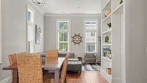A dining area with a wooden table and wicker chairs, a gray sofa, and a bookshelf with decorative items. - Coastal Townhome Near Park with Parking by Lucky Savannah (Savannah)
