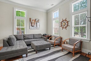 Un salon comprenant un canapé d’angle, deux fauteuils, un tapis et une roue de navire fixée au mur.
