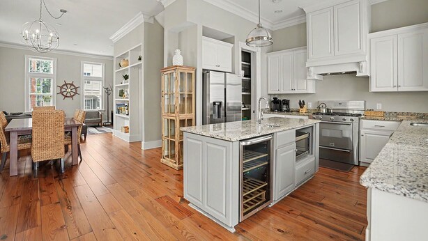 A modern kitchen with white cabinetry, a central island, stainless steel appliances, and a dining area with wicker chairs. - Coastal Townhome Near Park with Parking by Lucky Savannah (Savannah)