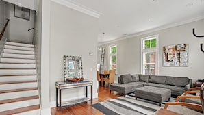 A living room with a gray sectional sofa, a wooden dining table, and a staircase with white railings. - Coastal Townhome Near Park with Parking by Lucky Savannah (Savannah)