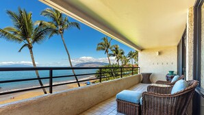 A balcony with wicker furniture, a view of the beach, and palm trees. - Beachfront condo Wailea w/ lanai and pool access (Wailea)