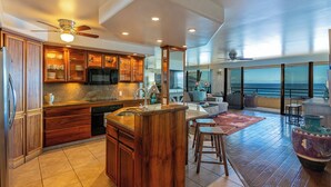A spacious kitchen with wooden cabinets, a central island, and a large window overlooking the ocean. - Beachfront condo Wailea w/ lanai and pool access (Wailea)