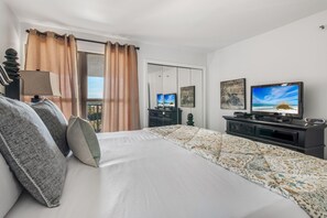 A hotel room with a bed, a TV, a dresser, and a window with curtains. - Golf Cart ~ Gulf Views ~ Private Balcony (Miramar Beach)