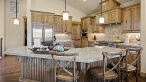 Une cuisine spacieuse avec des meubles en bois, un grand îlot central doté de tabourets, des appareils électroménagers en acier inoxydable et un éclairage suspendu.