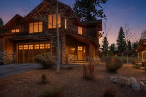 A large log cabin with a stone foundation, multiple windows, and a well-lit front porch.