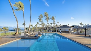 A clear blue pool with lounge chairs, palm trees, and a view of the ocean.