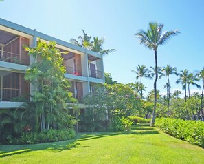 Um hotel moderno com estrutura em dois andares, varandas com plantas e um jardim bem cuidado com palmeiras e arbustos.