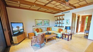 A spacious living room with a large flat-screen TV, a sofa set, a coffee table, and a wooden ceiling.