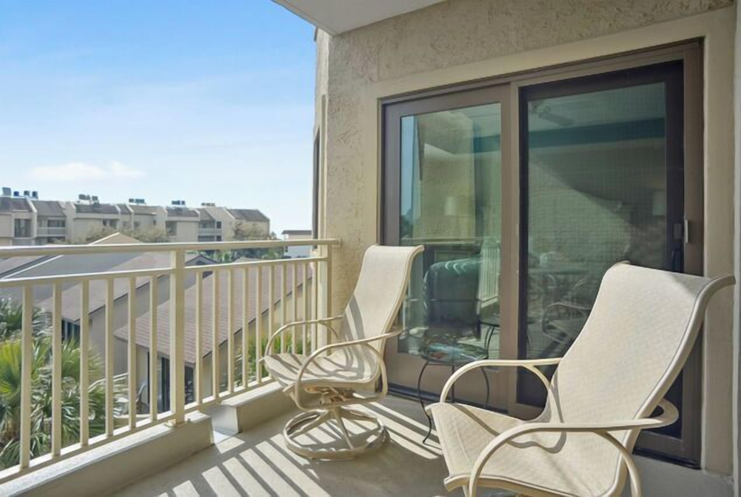 A balcony with two white chairs, a glass door, and a view of neighboring buildings.