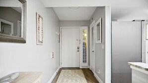 A hallway with a wooden floor, a patterned rug, a white door, and a refrigerator. - Surf Court 62 - Forest Beach 1st Floor Flat (Hilton Head Island)
