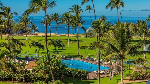 Uma área de piscina com palmeiras, vista para o oceano e um campo de golfe ao fundo.
