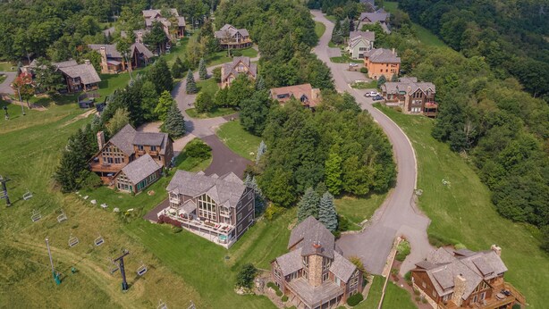 Vista aérea de uma área residencial com várias casas, uma estrada sinuosa e um teleférico.