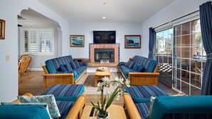 Ein Wohnzimmer mit Kamin, gestreifte Sofas, einem Couchtisch und Blick durch eine Glasschiebetür.