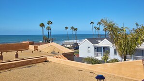 Eine Küstenlandschaft mit Strand, Palmen und einem kleinen weißen Haus mit Balkon.