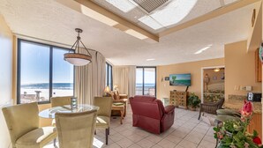 Een ruime woonkamer met uitzicht op het strand, een eethoek met een ronde tafel en een rode relax fauteuil.